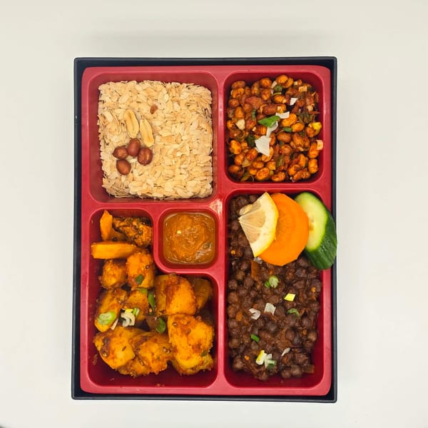 A red bento box filled with various Nepalese dishes, including flattened rice, spiced chickpeas, and potatoes.