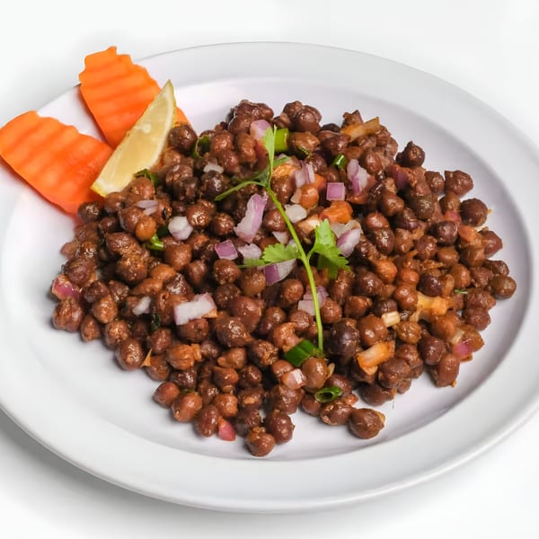 Nepalese black chickpeas with red onions, cilantro, and a lemon wedge on a white plate.
