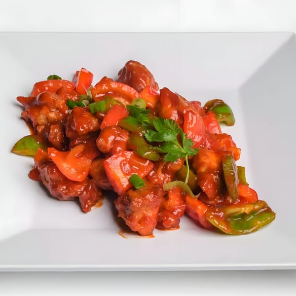 Nepalese chili chicken with red and green bell peppers, garnished with cilantro on a white plate.