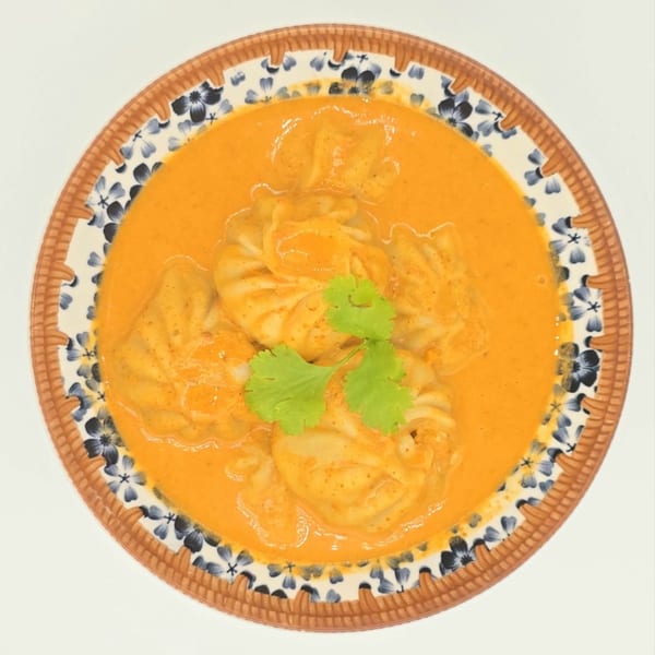 Nepalese momos in a rich orange sauce, garnished with fresh cilantro in a decorative bowl.