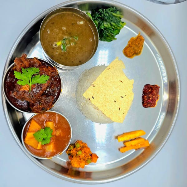 A Nepalese thali with rice, dal, chicken curry, vegetable curry, saag, pickle, and papad.