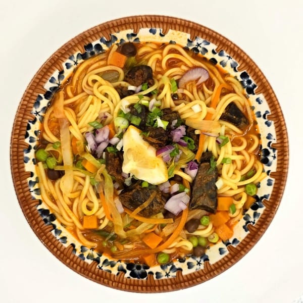 A close-up of a bowl of Nepalese thukpa noodles with vegetables, meat, and a lemon wedge.