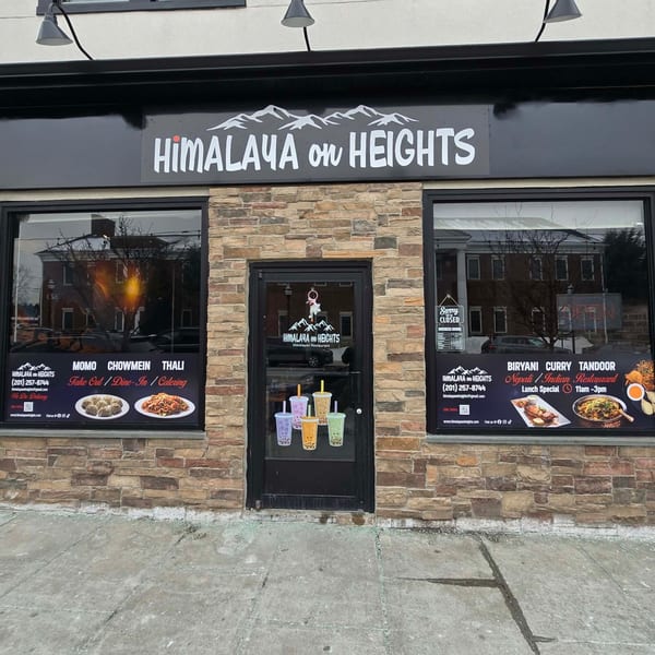Exterior of Himalaya on Heights restaurant with a black sign, stone facade, and window advertisements.